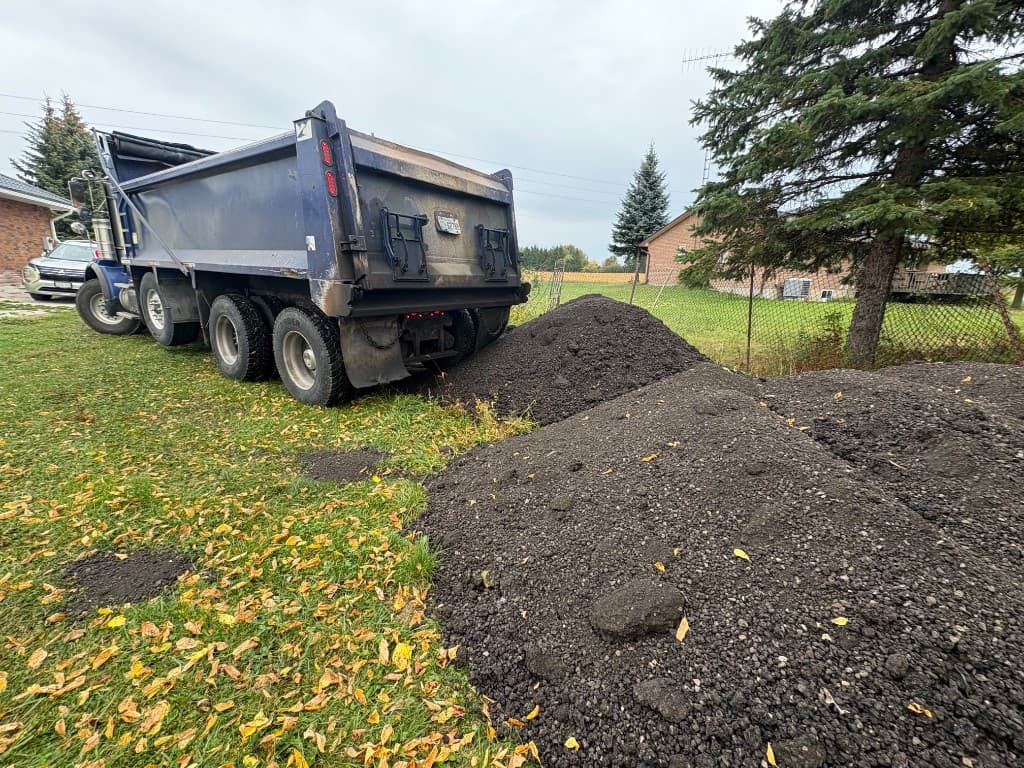 Asphalt millings unloaded from the back of a dump truck onto the site of the new parking area