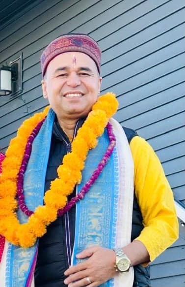 Pandit Mahesh Kumar Acharya wearing a marigold garland and a traditional cap